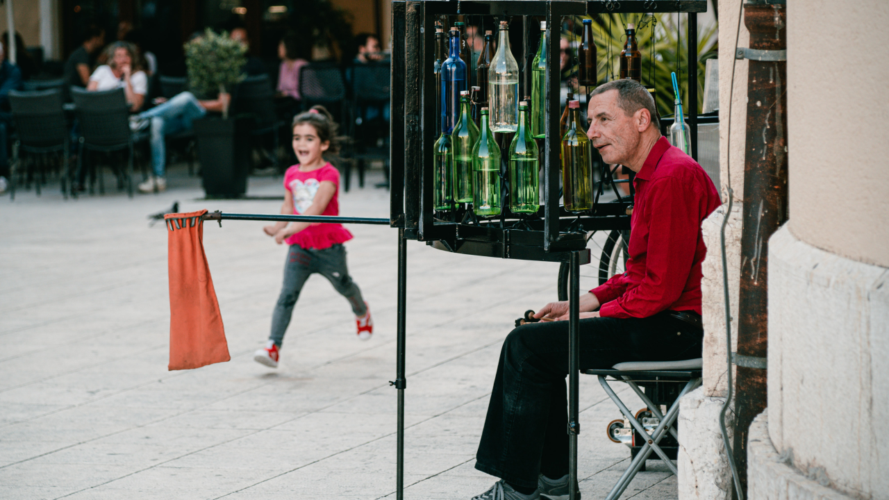 Ljetna atmosfera ispred kazališta uz uličnog svirača koji svira boce